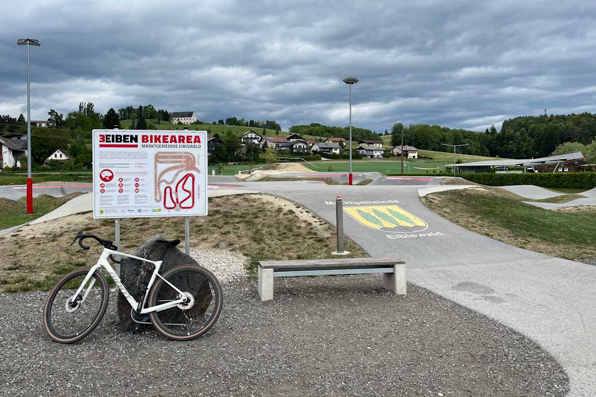 Der „3Eiben Pumptrack“ in Eibiswald: Übersichtstafel und angelehntes Rad vor dem Gelände des Pumptracks