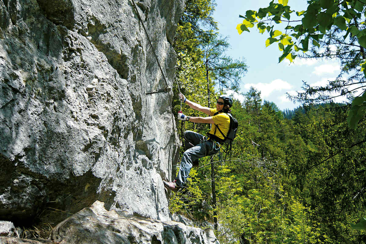 Mann hängt an vertikaler Felswand im Klettersteig Zahme Gams in Salzburg