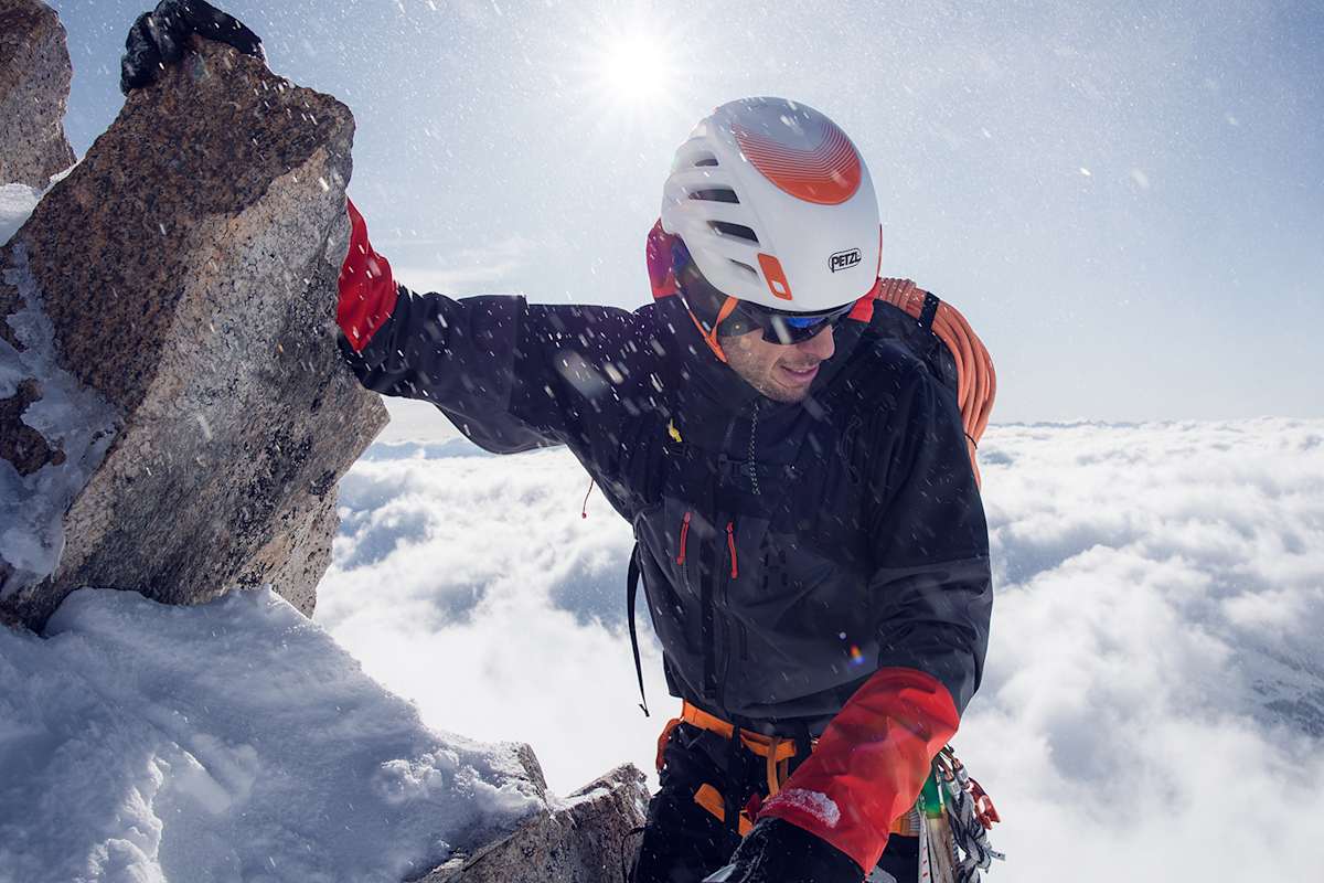 mann beim bergsteigen auf bergspitze, gekleidet in haglöfs
