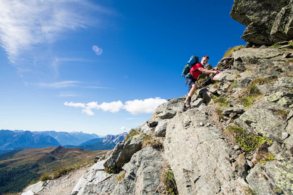Wanderer mit Stöcken in der Hand klettert über felsige Passage am Karnischen Höhenweg