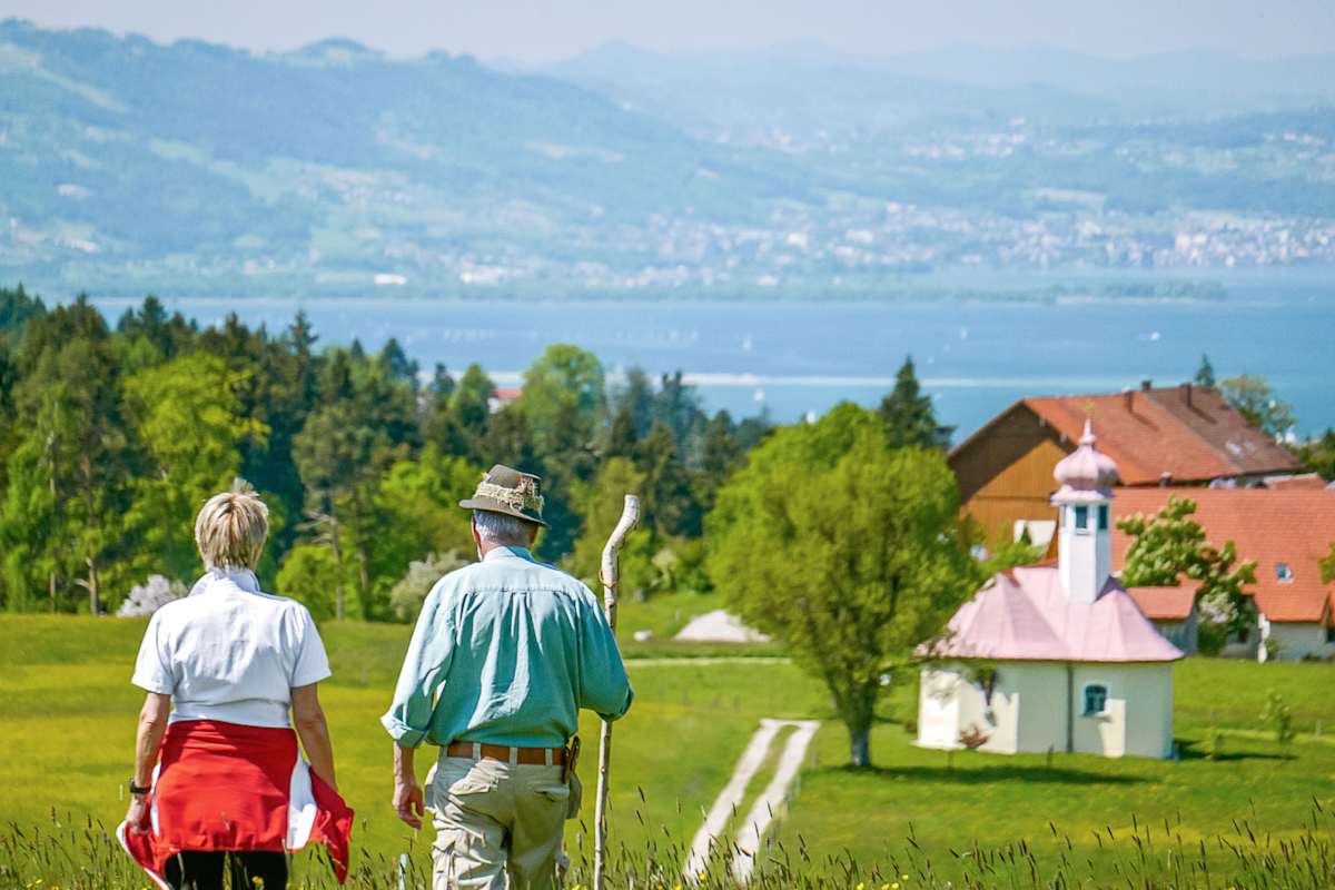 Ein Mann und eine Frau wandern in Scheidegg mit Blick auf den Bodensee.