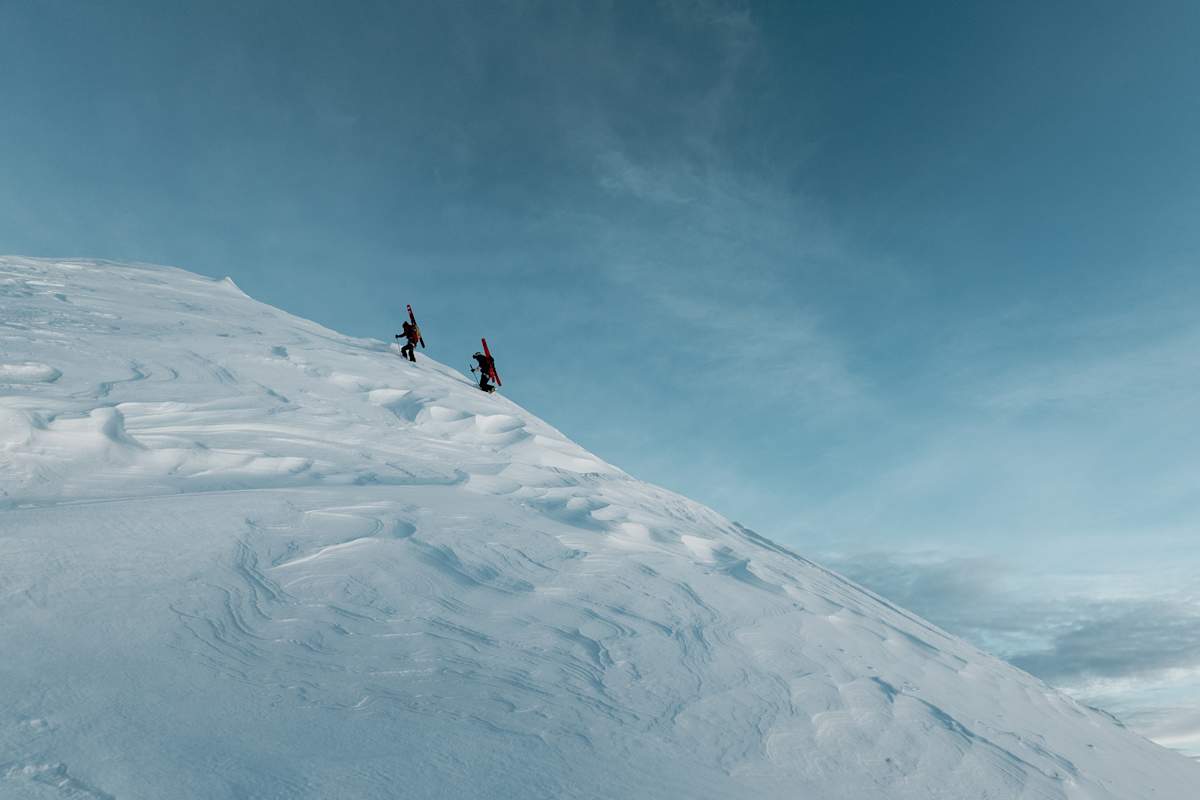 Zwei Skitourengeher gehen einen unberührten Schneehang hinauf.