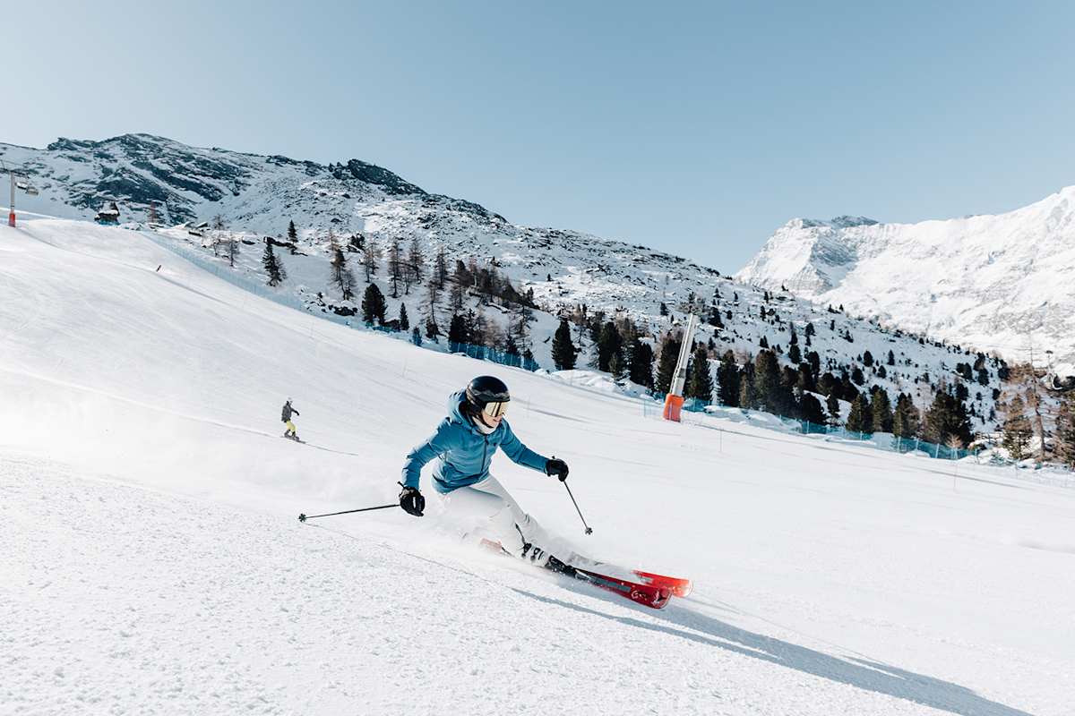 Eine Frau fährt eine Skipiste in der Meraner Bergwelt hinunter. Die Landschaft ist tiefverschneit.