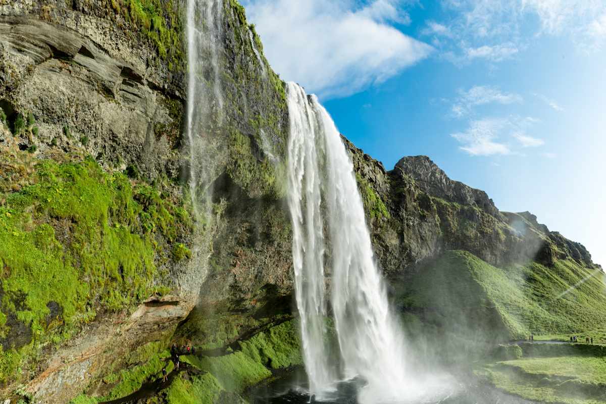 Der Seljalandsfoss an bewachsener Felsklippe vor blauem Himmel