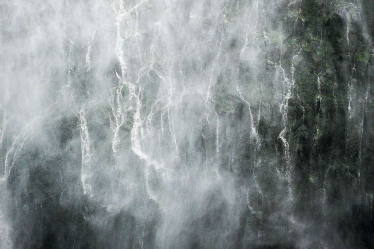 Gischt vor steilem Felshang mit Wasserfällen