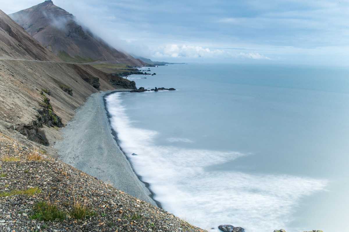 Schroffe Berge mit Kiesstrand und grau-blauem Meer