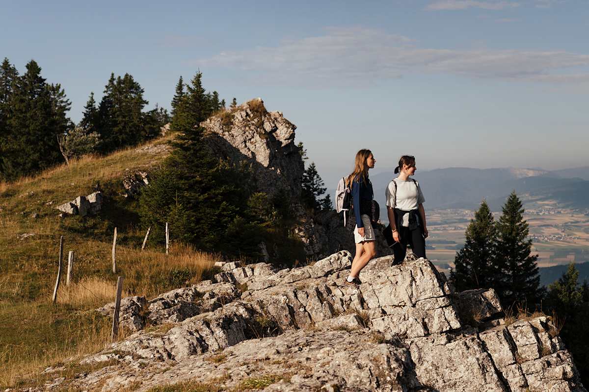 Zwei Frauen wandern auf einem felsigen Gipfel an einem sonnigen Tag.
