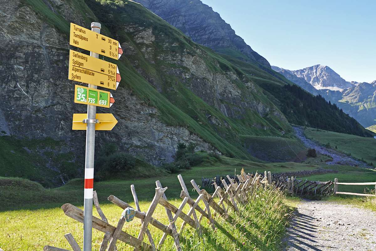 Zu sehen ist ein Schotterweg auf der Via Capricorn mit einer sommmerlichen alpinen Lanschaft im Hintergrund.