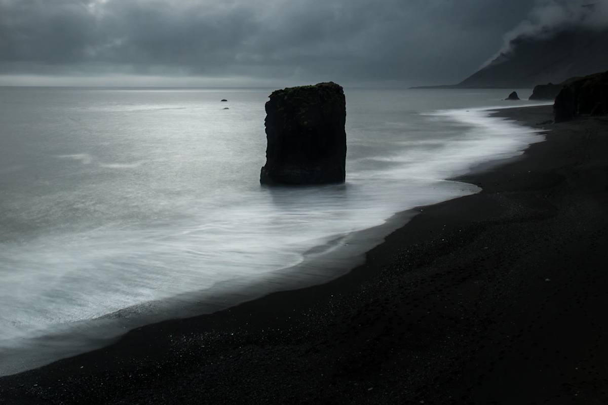 Ein einsamer Felsturm im Meer am schwarzen Strand