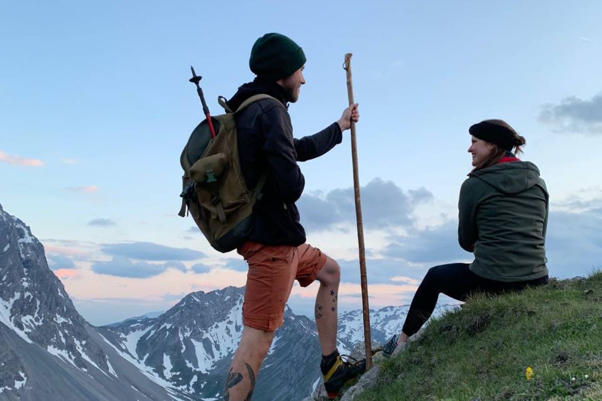 zwei Personen sitzen bzw. stehen im Abendlicht auf einem Berghang