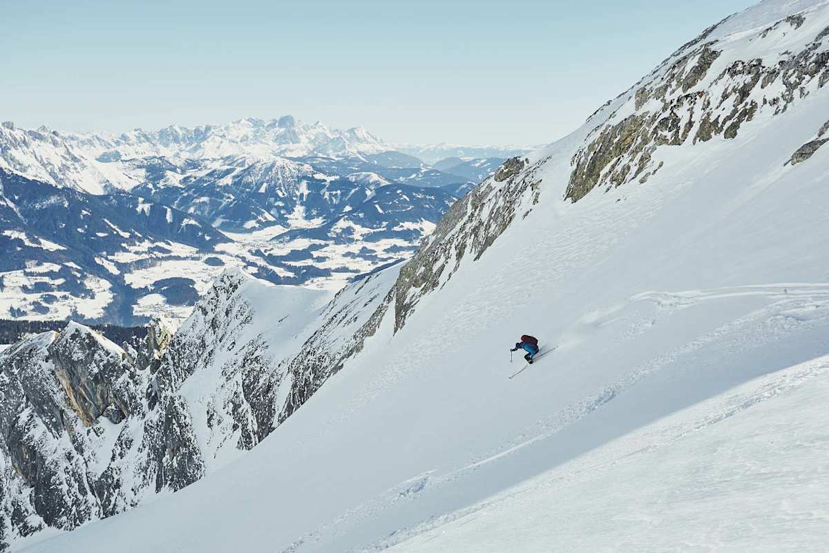 Ein Skifahrer bei der Abfahrt in einer Rinne, dahinter der Alpenhauptkamm.
