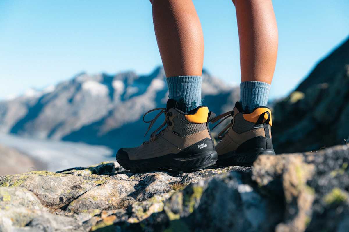 Beine von Wanderern in robusten Bergschuhen von Hanwag – im Hintergrund Berge und Gletscher