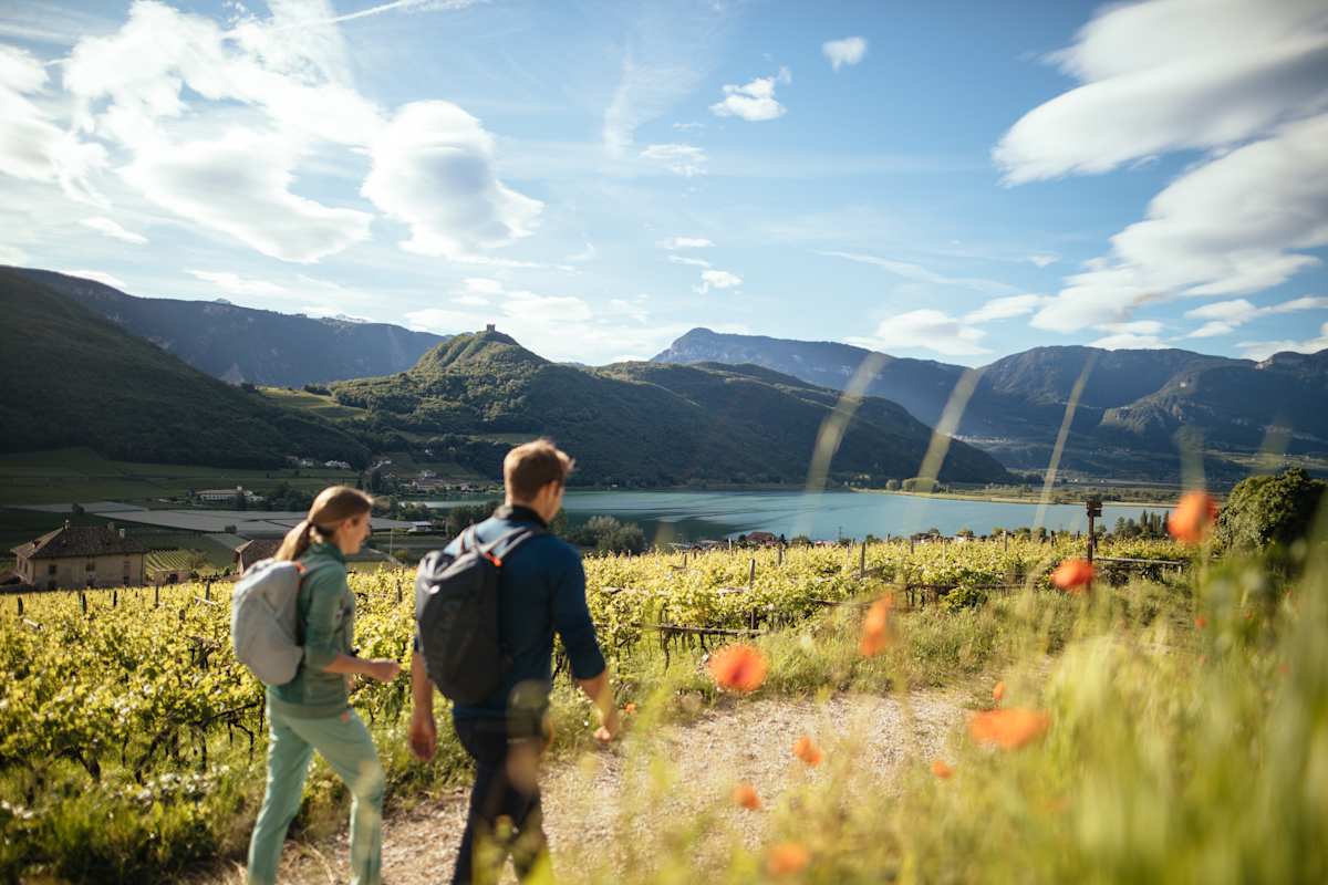 Ein Pärchen wandert auf einem Weg zwischen Weinbergen mit Blick auf den Kalterer See in Südtirol.