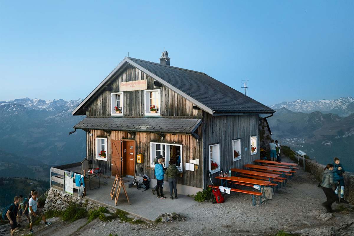 Ein Berggasthof bei Sonnenaufgang, dahinter die Berge.