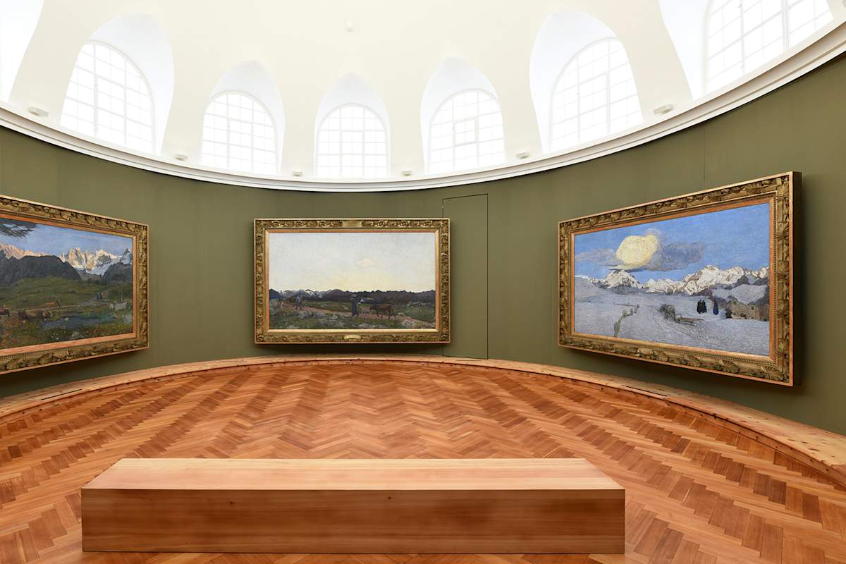 Man sieht das Innere des Segantini Museums in St. Moritz, mit drei Gemälden des Künstlers die an einer grünen Wand hängen.