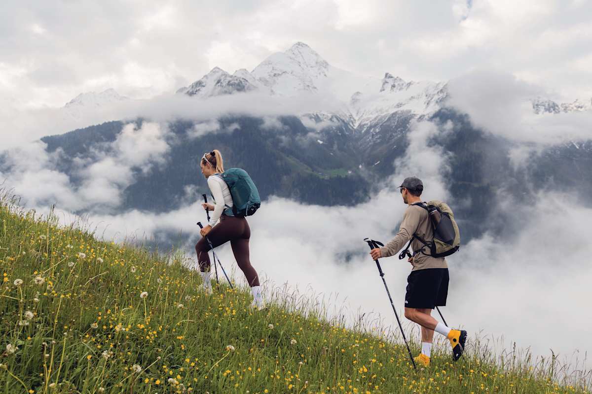 Zwei Personen wandern durch eine Blumenwiese.