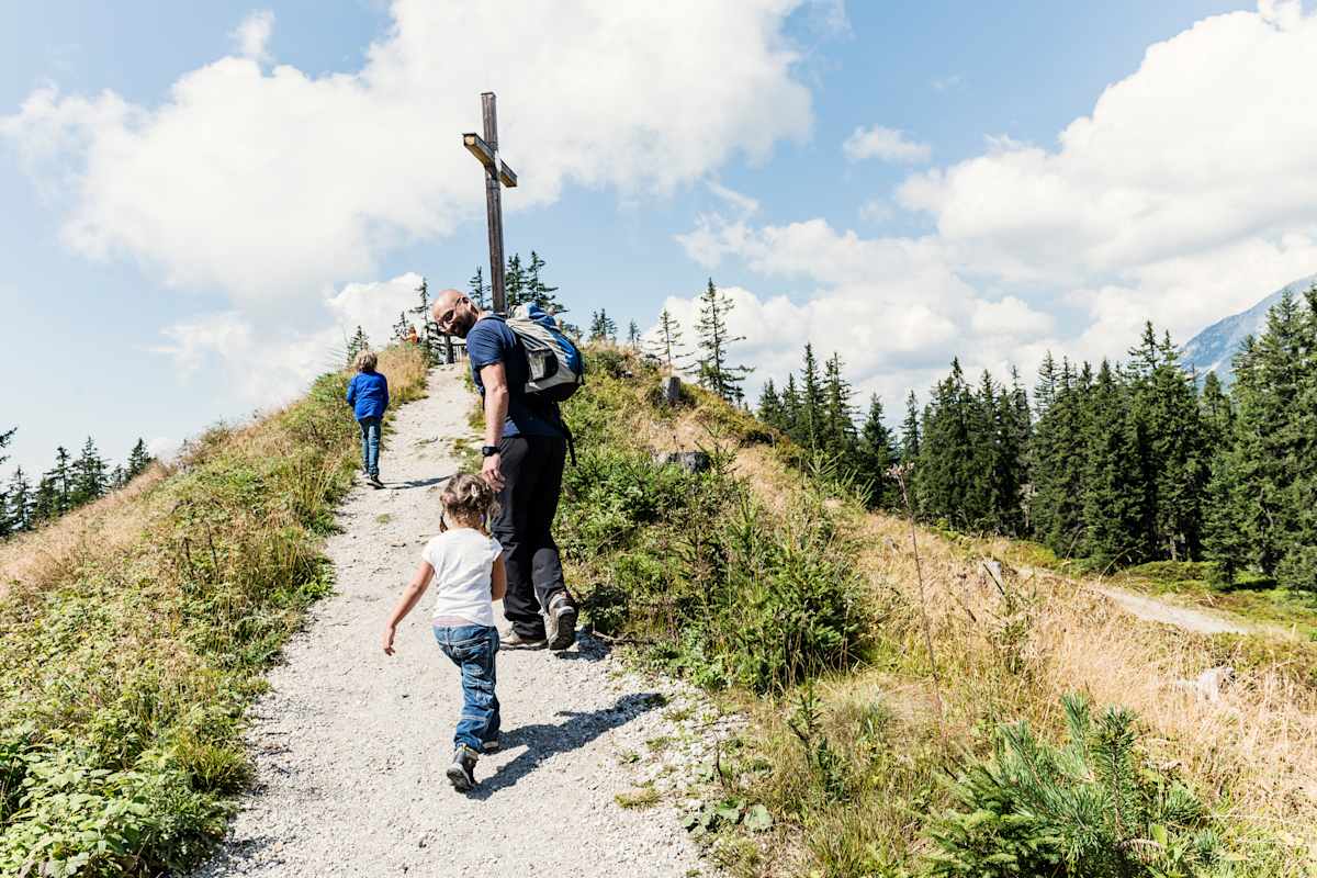 Die drei Wanderer haben das Gipfelkreuz erreicht.
