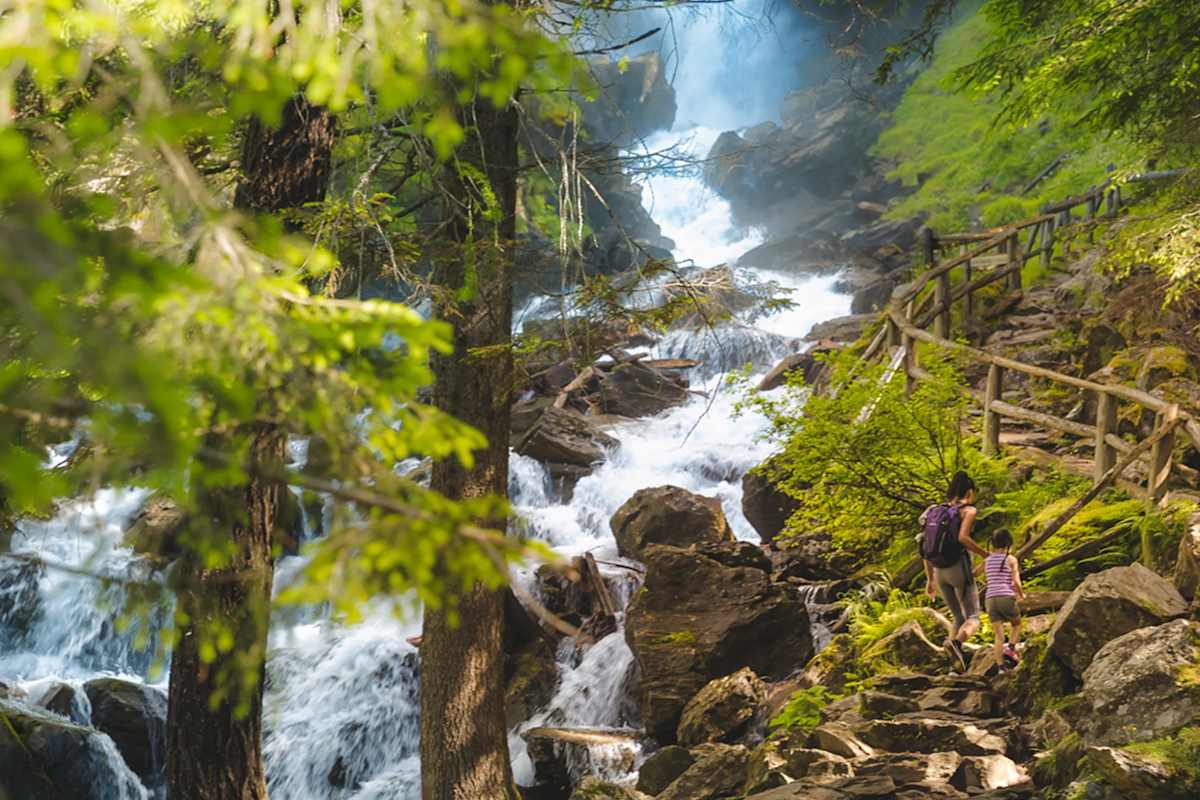 Eine Mutter und ihre Tochter steigen einen steilen Steig neben einem tosenden Wildbach empor.