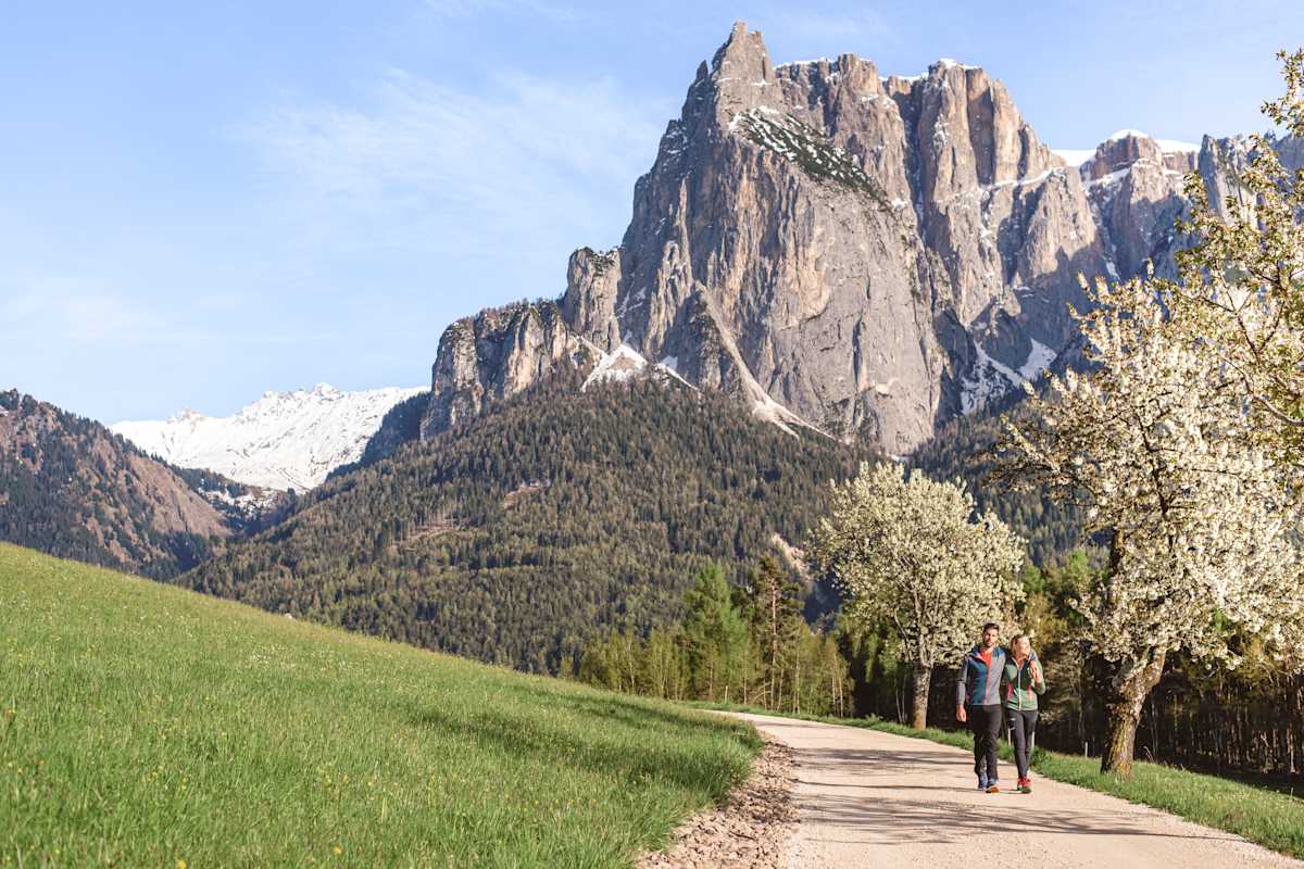 Ein Mann und eine Frau spazieren eng umschlungen durch eine frühlingshafte Landschaft auf der Seiser Alm.