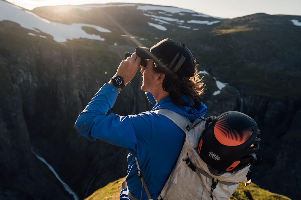 Ein Mann steht mit Fernglas auf einem Wanderpfad und sieht in die Ferne