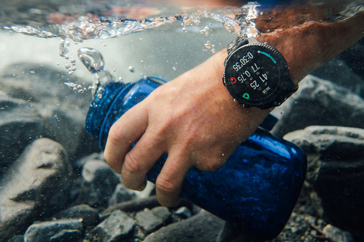 Ein Mann trägt eine Suunto Uhr und hält sie in einen Bach unter Wasser