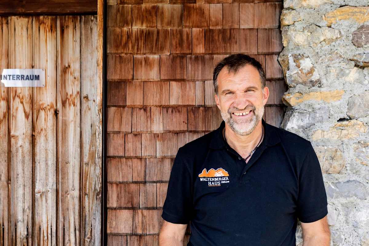 Ein Portrait des Hüttenwirts Markus vor einer Holzschindelwand