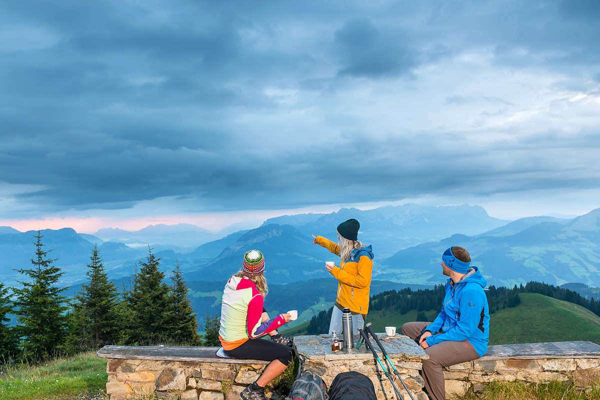 Drei Personen sitzen auf einer Bank und bewundern das alpine Panorama, das sich vor ihnen ausbreitet.