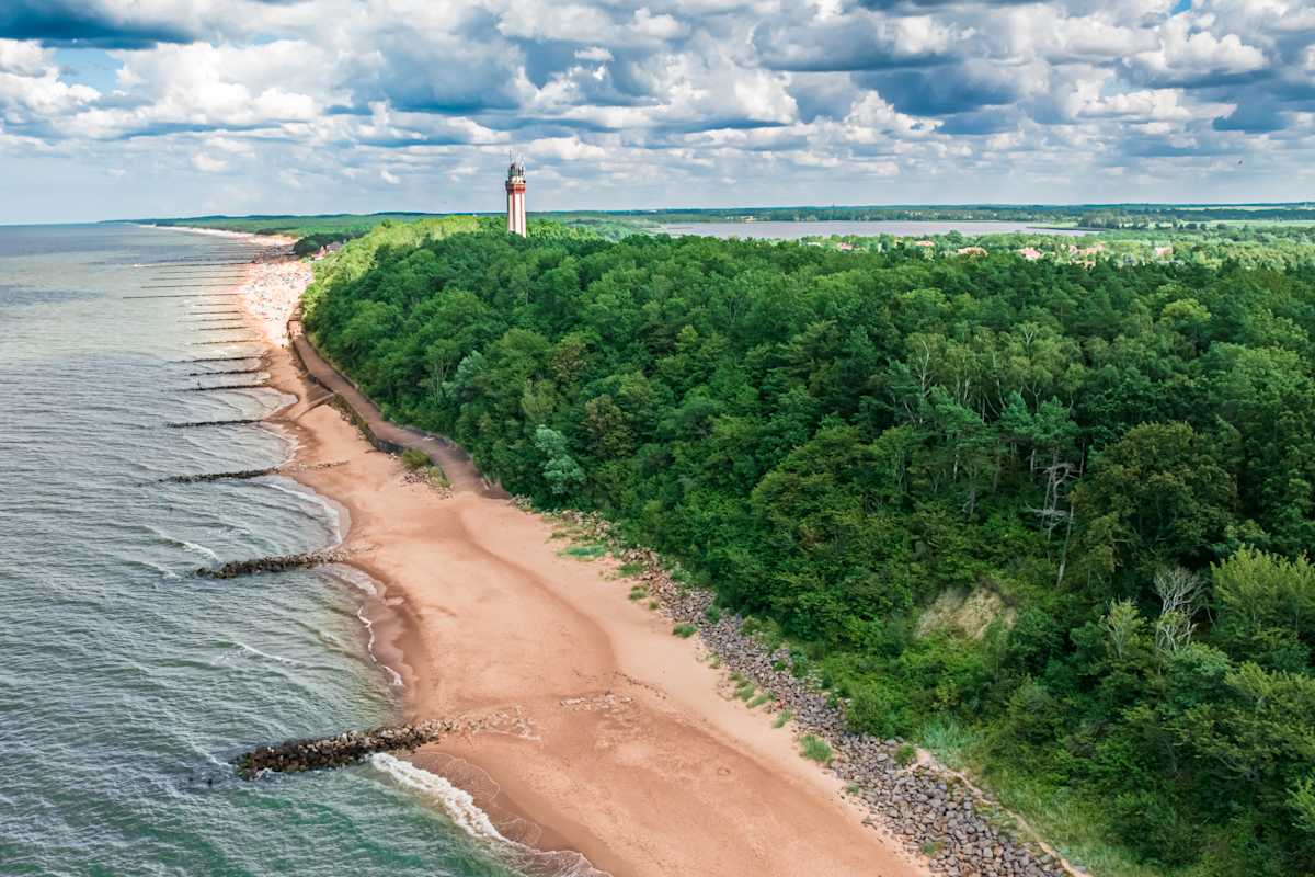 Eine Küste mit rotem Sand, Wald, See und Leuchtturm.
