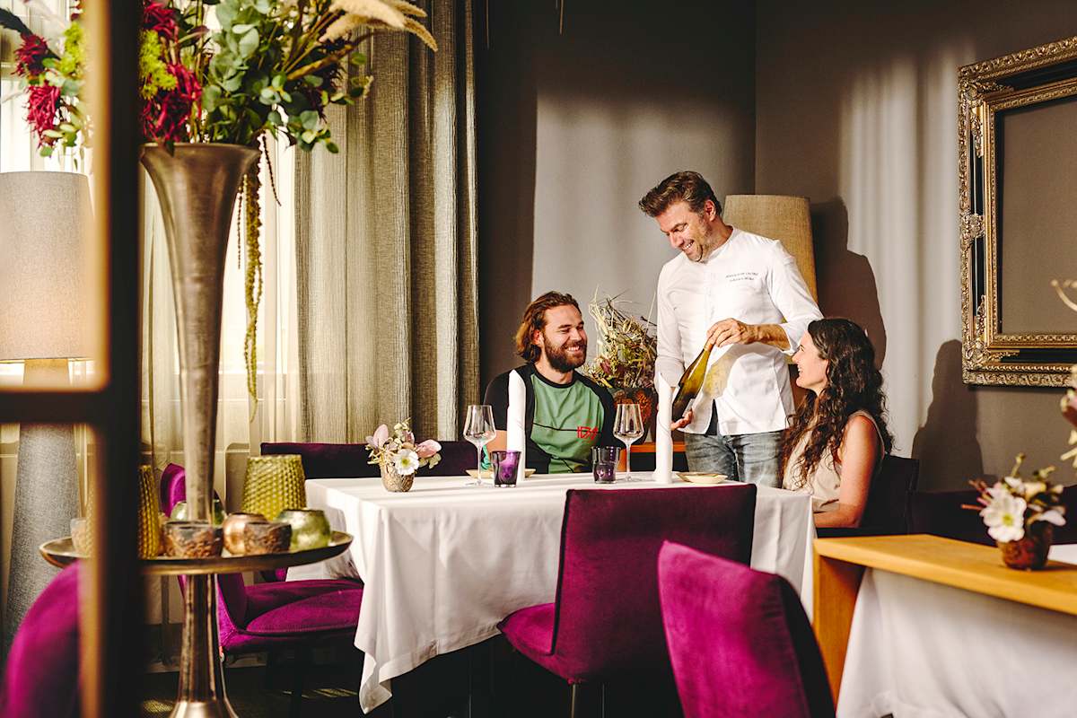 Der Spitzenkoch schenkt Wein für zwei Gäste in einem eleganten Restaurant mit gemütlicher Atmosphäre ein.