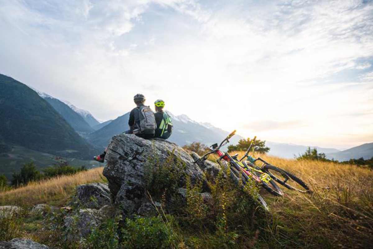 Mountainbiker genießen den Ausblick am Vinschger Sonnenberg bei Sonnenuntergang.
