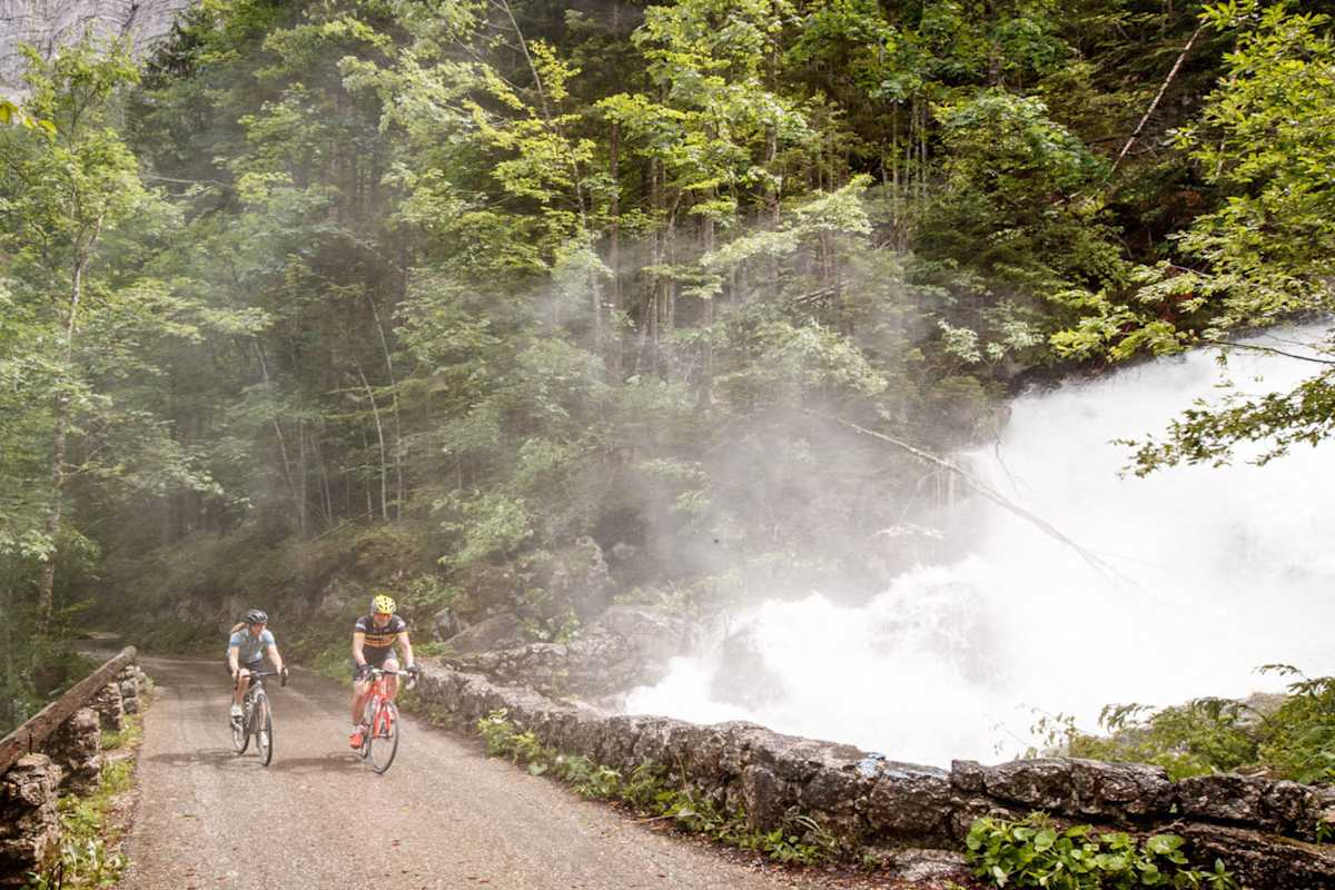Zwei Gravelbiker radeln auf einem Forstweg durch den Wald.