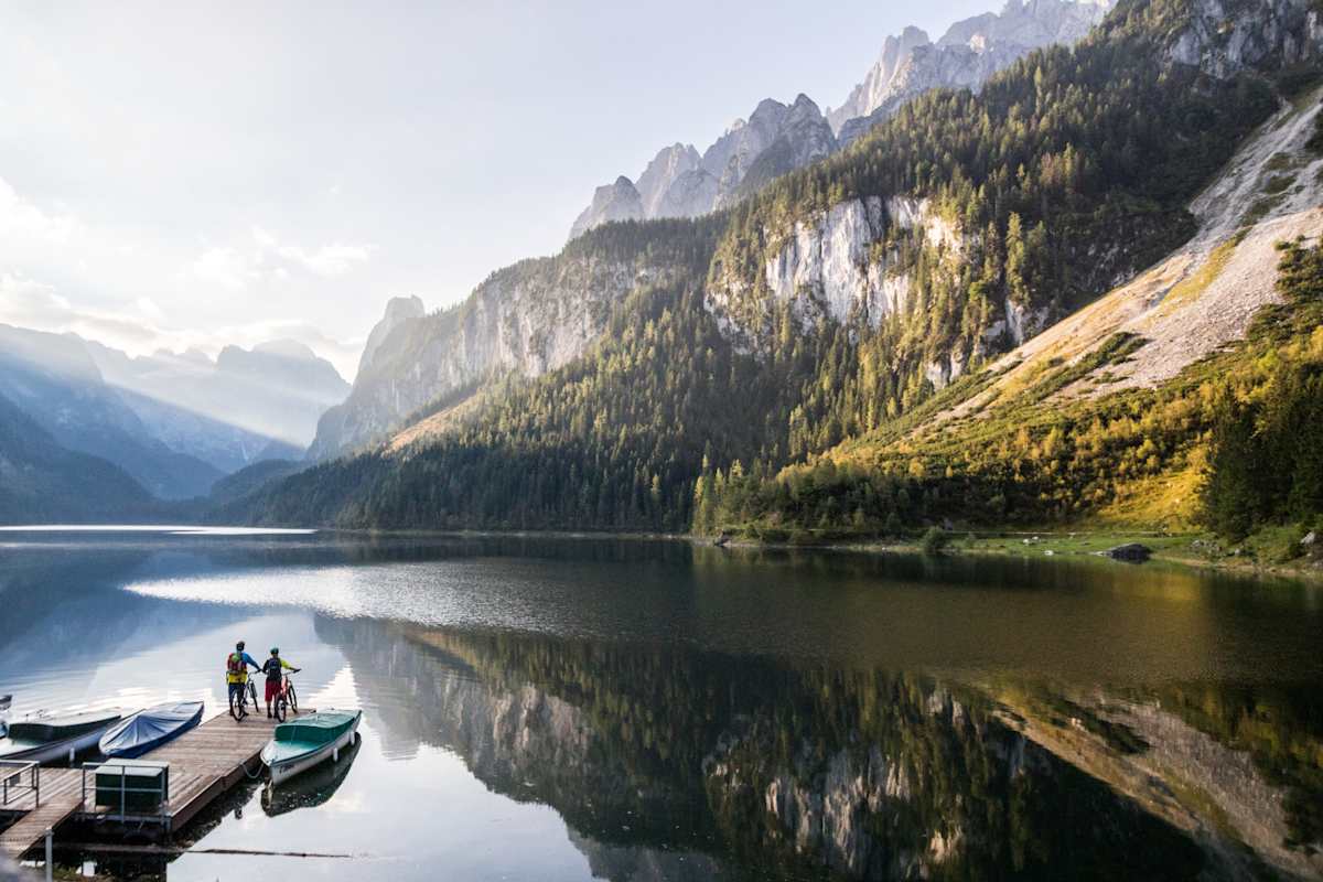 Zwei Radfahrer auf einem Steg vor dem Gosausee, im Hintergrund der Dachstein.