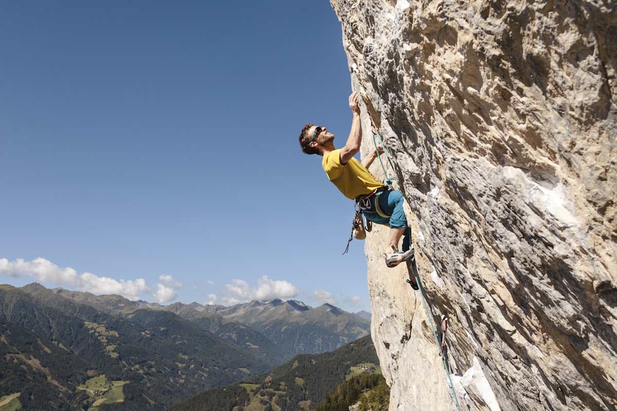 Ein Kletterer macht sich auf den Weg auf die Bergspitze und hängt an der Felswand.