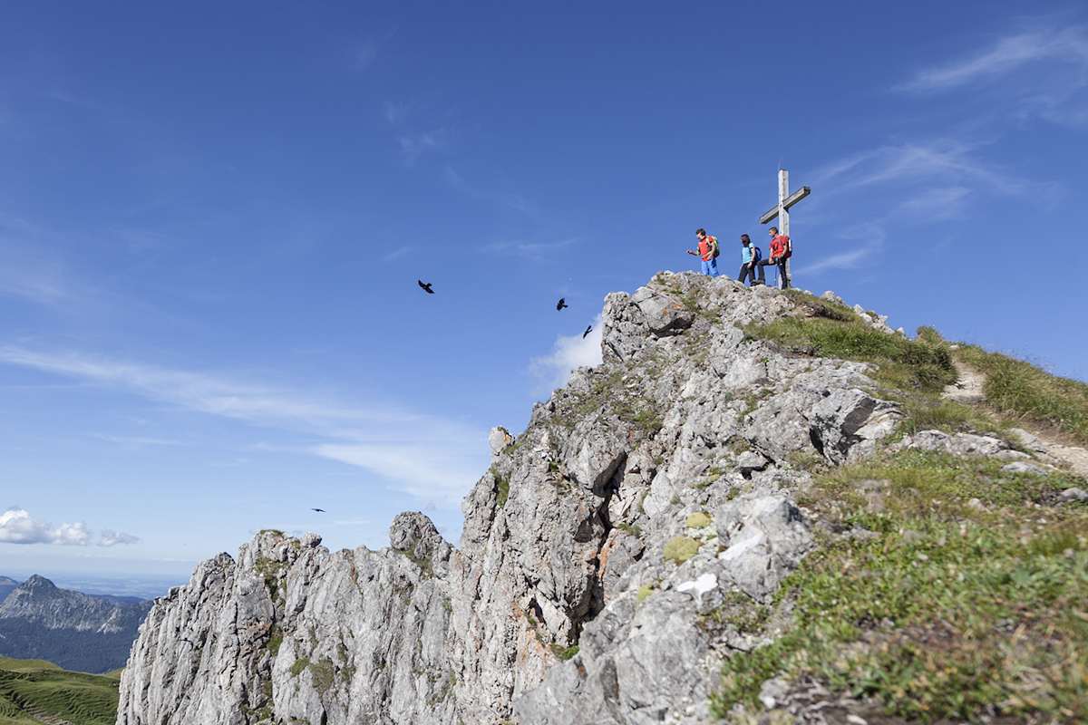 Drei Wanderer auf dem Gipfelkreuz in Tirol