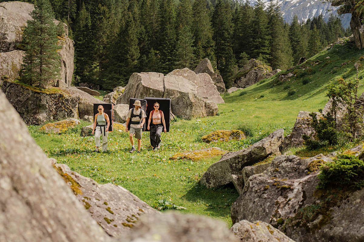 Drei Wanderer gehen auf einer Wiese, umgeben von Bergen