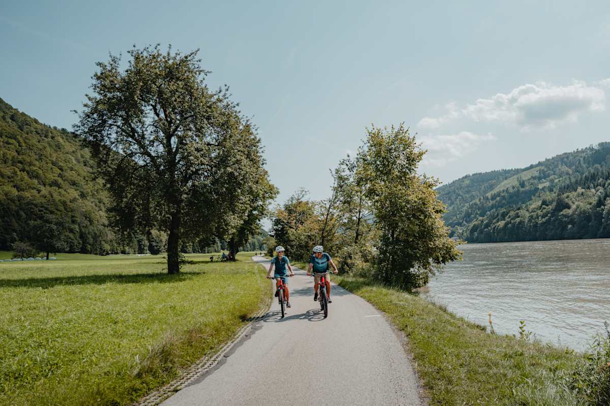 Zwei Radfahrer radeln an der Donau entlang.