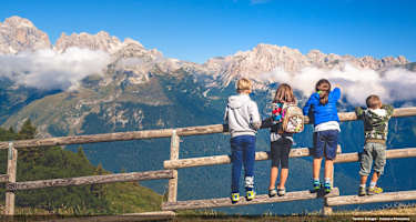 Drei Kinder stehen auf einem Holzzaun und blicken in die Berge.