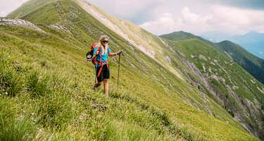 Wanderin geht mit Wanderstöcken über begrasten Berg