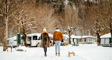 Ein Pärchen geht mit einem Rodel über einen Campingplatz im Winter.