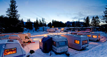 Der Wintercampingplatz Jaunpass bei Nacht. Es liegt Schnee und die Wohnwagen sind hell erleuchtet.