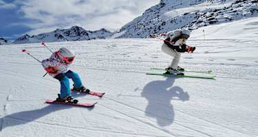 Eine Frau und ein Mädchen fahren gemeinsam Ski und nehmen dabei die Schussposition ein.