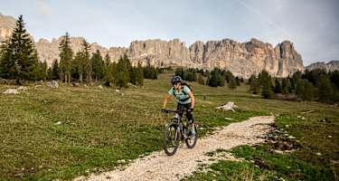 Eine Frau fährt auf einem Mountainbike. Hinter ihr liegt ein Dolomitenpanorama.