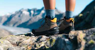 Beine von Wanderern in robusten Bergschuhen von Hanwag – im Hintergrund Berge und Gletscher