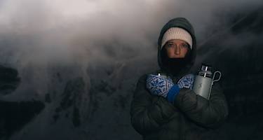 Person in Winterkleidung mit Thermosflasche Hydro Flask Hot Flask & Cup in verschneiter Berglandschaft bei Nebel und eisigen Temperaturen.