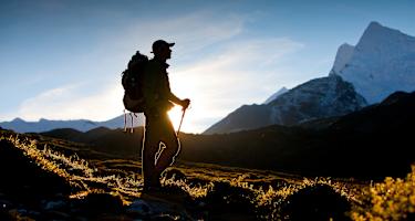Ein Wanderer im Gegenlicht. Im Hintergrund ein schneebedeckter Berg.