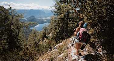 Eine Wandrerin mit Rucksack und Ausrüstung, die durch den Wald auf den Altauseer See hinunterblickt.
