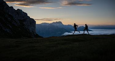Zwei Trailrunner laufen im Morgengrauen am Berg.