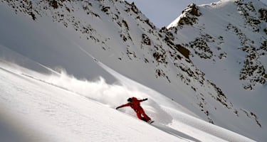 Eine Person fährt Snowboard im Schnee auf einem Berg in roter Ausrüstung.