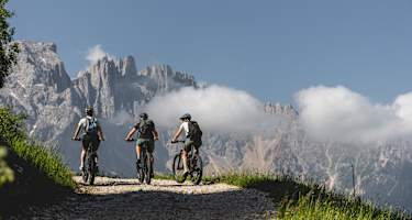 Drei Mountainbiker auf der Latemar Ronda im Eggental vor der Kulisse des Latemar Massivs.