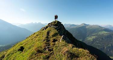 Zwei Personen stehen auf einem spitzen Bergkamm oberhalb von Lenzerheide mit schöner Aussicht